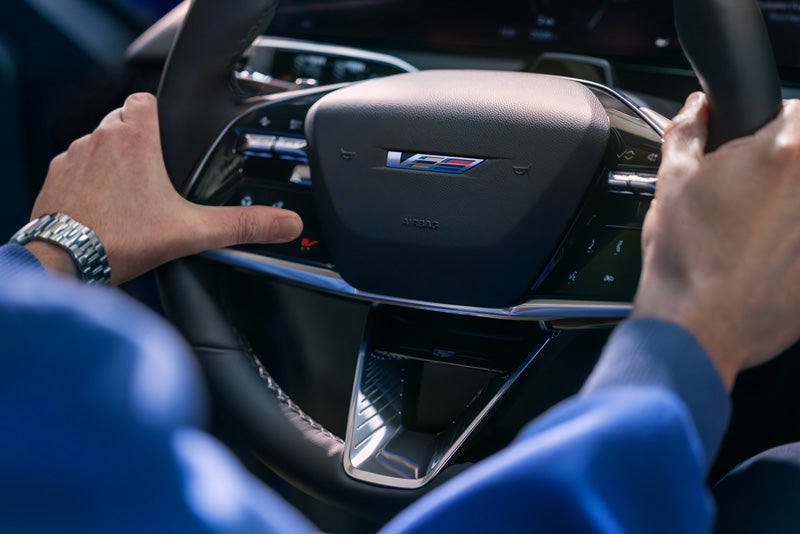 Close-up of a Man About to Press the V-Button on the 2026 OPTIQ-V Steering Wheel | Three-Way Cadillac in Bakersfield CA
